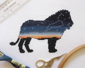 Cross stitch picture of the silhouette of a lion, filled with a sunset scene and an accurate depiction of the constellation Leo