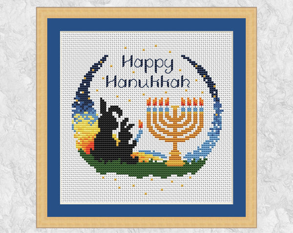 Happy Hanukkah Bunnies cross stitch pattern. Two bunnies lighting a menorah at sunset with the words Happy Hanukkah. Shown in frame.