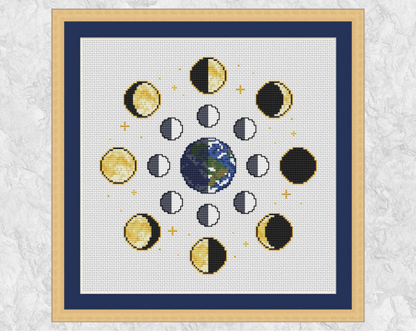 Moon Phases cross stitch pattern on white fabric. Shown with frame.