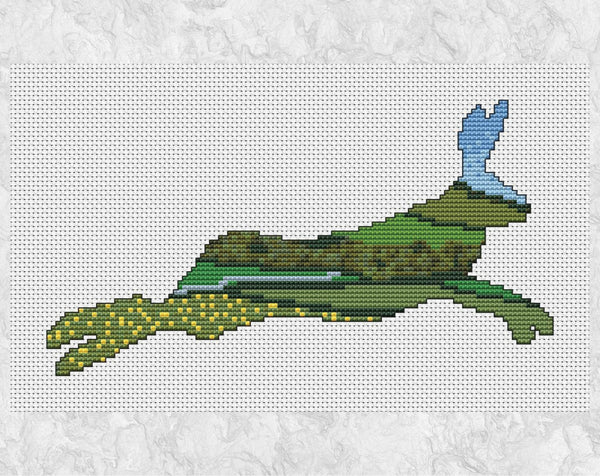 Cross stitch pattern of the silhouette of a running hare, filled with a scene of the British countryside with rolling hills, fields, farmland, buttercups, woodland and a river. Shown without frame.