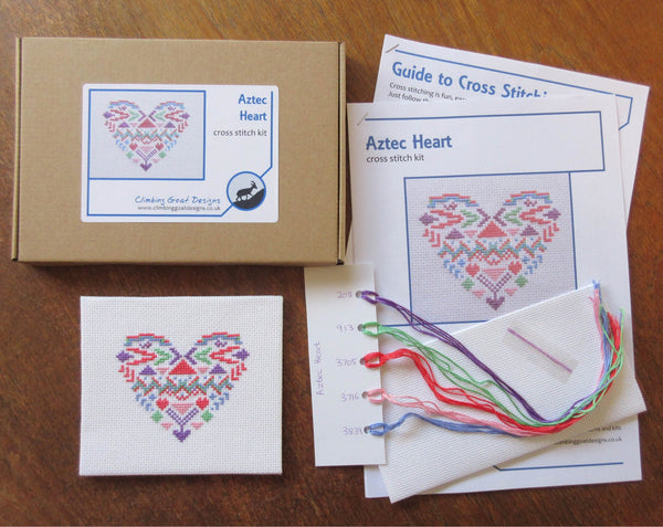 Aztec Heart cross stitch kit. Picture of contents: Labelled box, cross stitch instructions, pattern booklet, sorted thread card, fabric and needle. Complete stitched piece is also shown in the image.