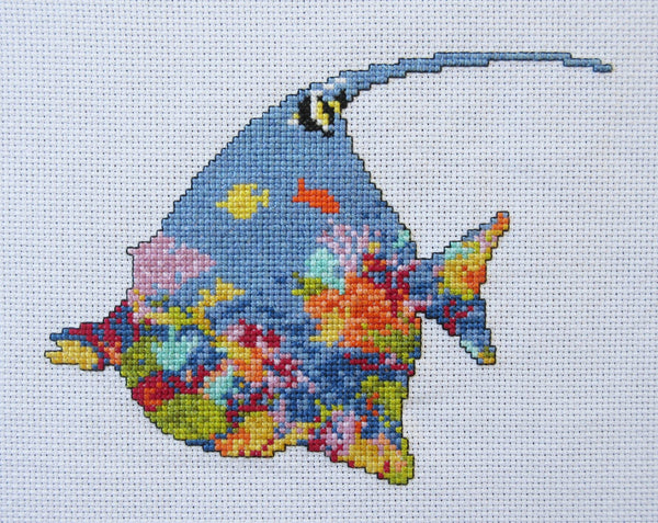 Cross stitch pattern of the silhouette of a tropical fish (a moorish idol fish) filled with a scene of a coral reef. Straight view of stitched piece.