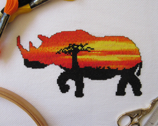 Cross stitch pattern of the silhouette of a rhinoceros filled with a view of an African sunset behind a baobab tree. Perfect for animal lovers.