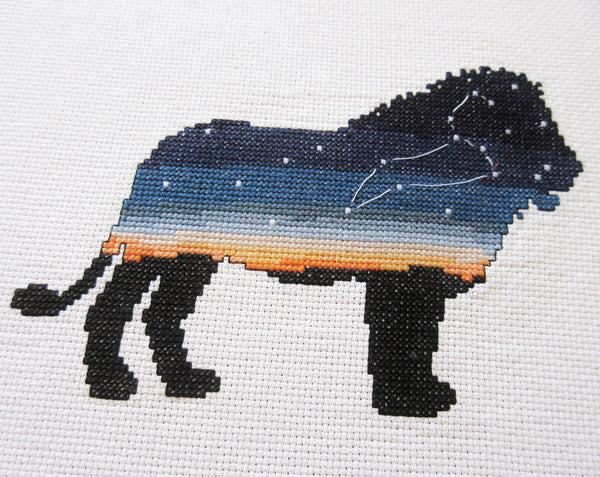 Leo Zodiac Lion cross stitch pattern - silhouette of lion filled with sky, sunset and the constellation of Leo. Angled view of stitched piece.