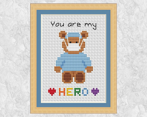 Cross stitch pattern of teddy bear wearing scrubs and face masks, with the words 'You are my HERO'. Shown in frame.