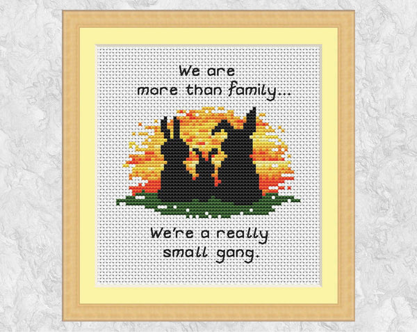Cross stitch pattern of three bunny silhouettes against a sunset, with the words "We are more than family... We're a really small gang.". Shown in frame.