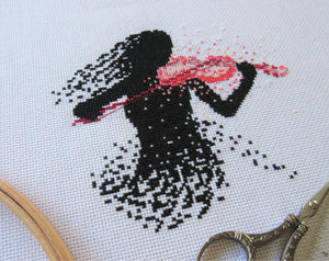 Cross stitch picture of the black silhouette of a female violinist playing a pink modern art violin
