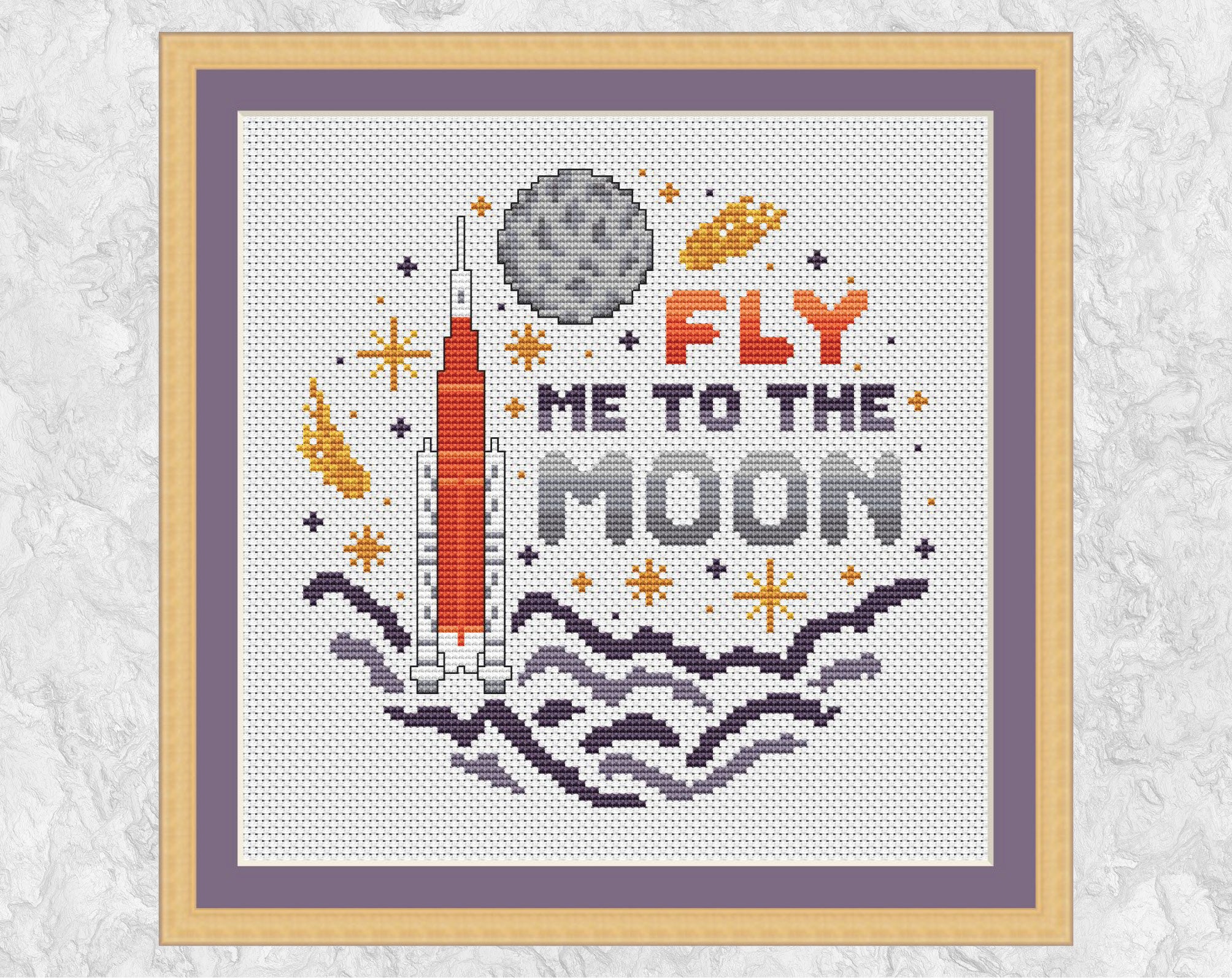 Fly Me To The Moon cross stitch pattern. Cartoon of Artemis rocket, Moon and stars. Shown in frame.
