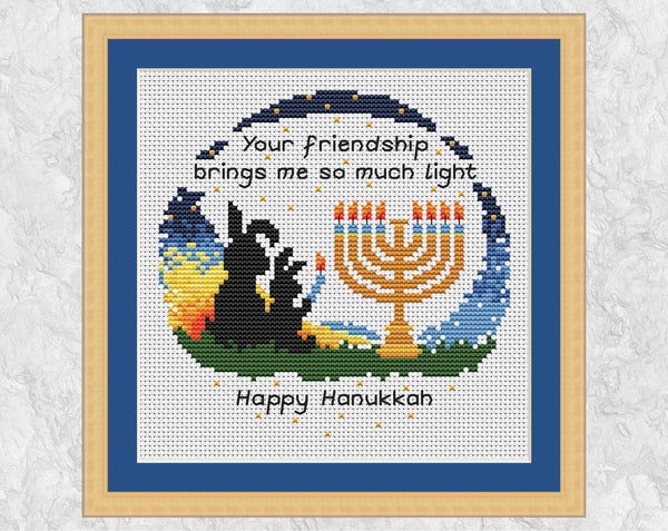 Hanukkah Friendship cross stitch pattern. Bunnies lighting a menorah with the words 'Your friendship brings me so much light - Happy Hanukkah'. Shown in frame.