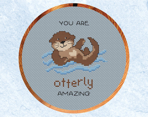 Otterly Amazing cross stitch pattern. Cartoon of an otter with the words "You are otterly amazing". Shown in six inch hoop.