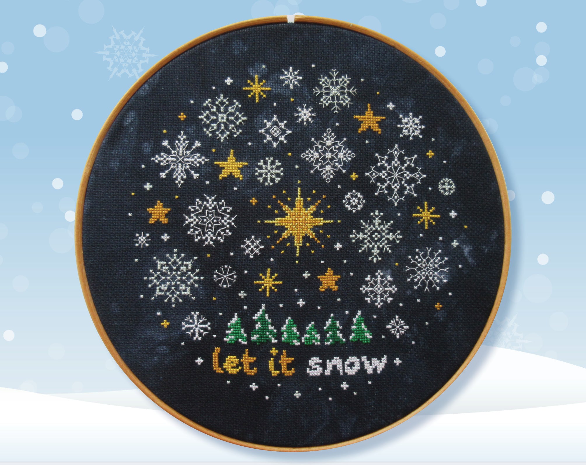Snowflakes and Stars cross stitch pattern. Intricate snowflakes and golden stars surrounding a large eight-pointed star, all above little snow-capped trees and the words 'let it snow'.