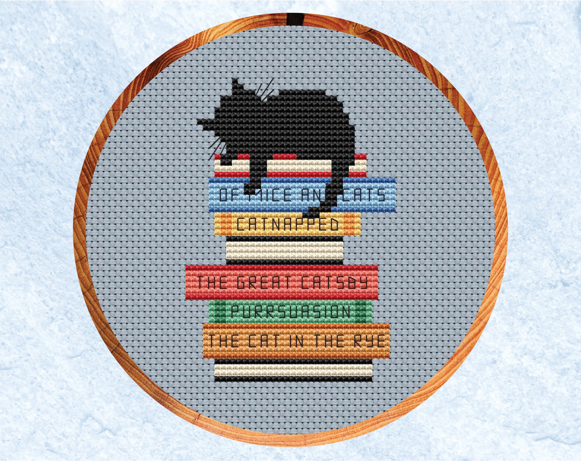 Catnapped cross stitch pattern. Black cat asleep on a pile of books with pun titles. Shown in hoop.