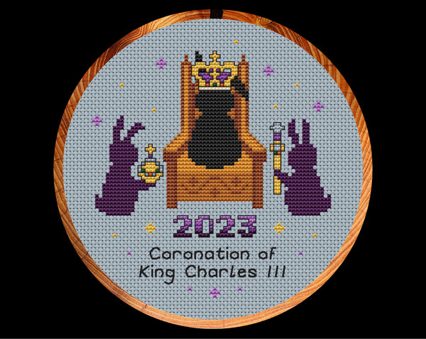 Coronation Bunnies cross stitch pattern. A bunny wearing a crown sits on a throne, with a bunny with an orb on one side and a bunny with a sceptre on the other. Shown in hoop.
