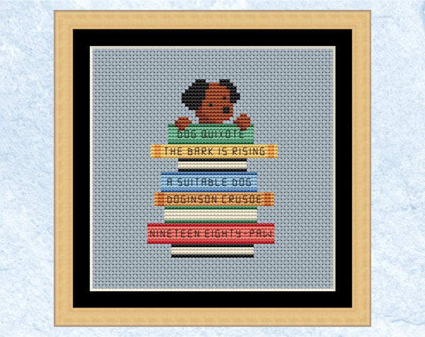 Cross stitch pattern of dog with its paws on a pile of books labelled with dog puns of classic book titles. Shown in frame.