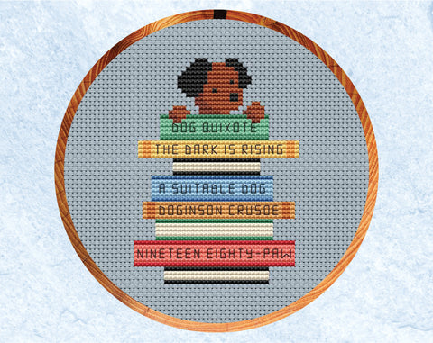 Cross stitch pattern of dog with its paws on a pile of books labelled with dog puns of classic book titles. Shown in hoop.