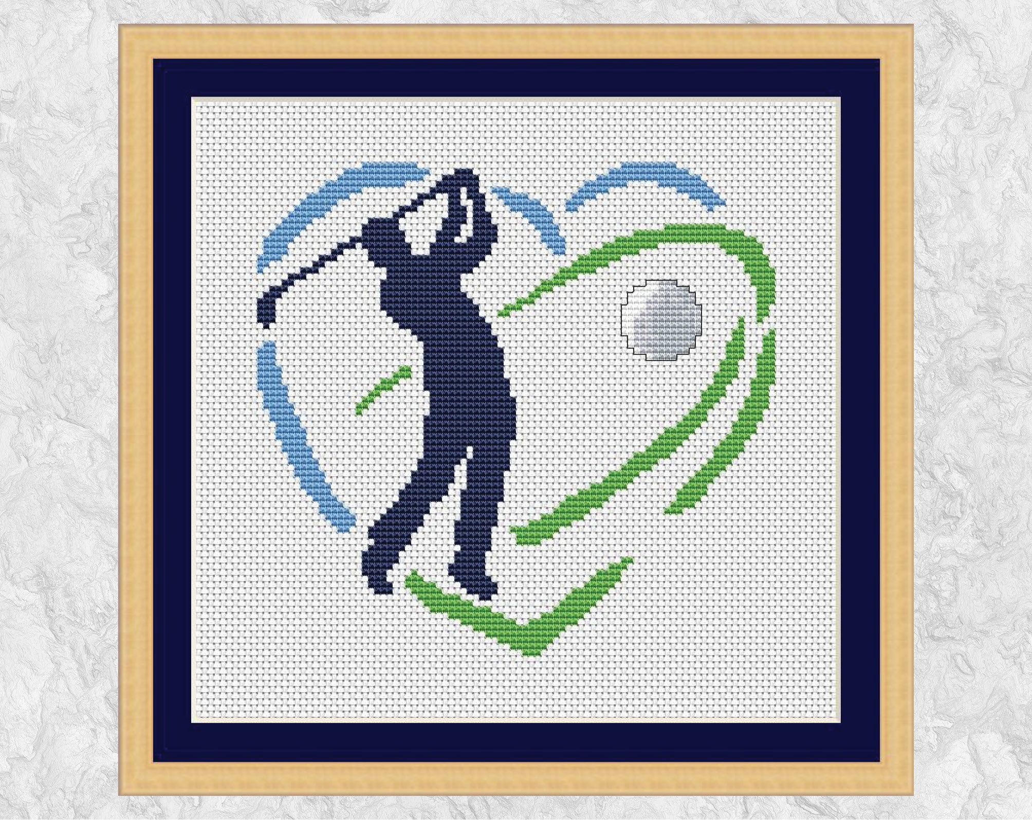 Golf Heart cross stitch pattern - silhouette of a golfer hitting a golf ball within a blue and green heart shape. Shown with frame.