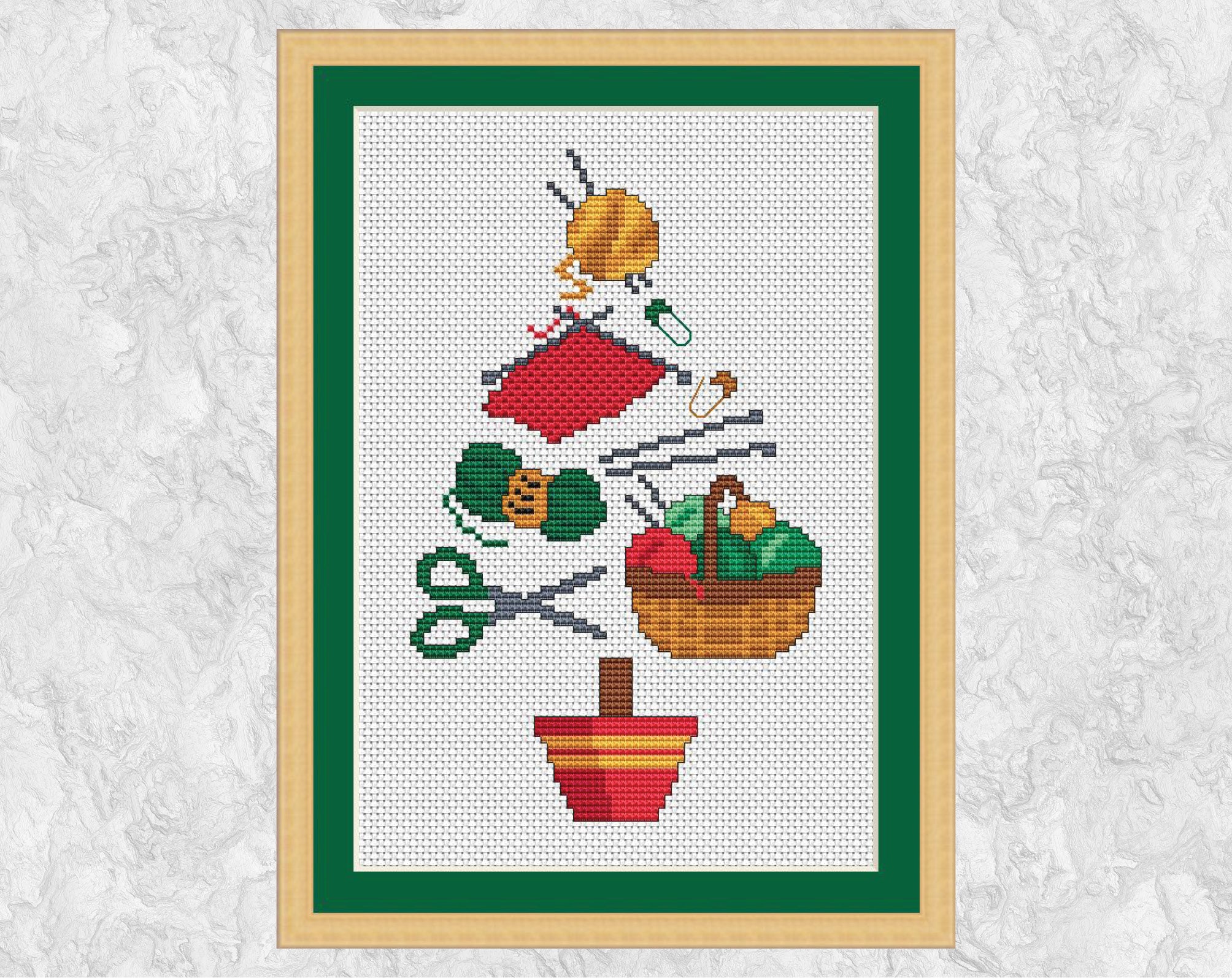 Knitting Christmas Tree cross stitch pattern. A Christmas tree shape made up of yarn, knitting, knitting needles, scissors, a basket of yarn and stitch markers. Shown with frame.