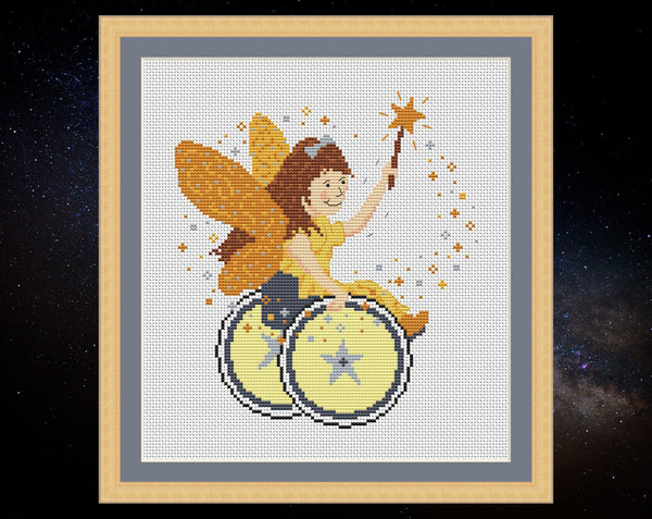 Magical Fairy cross stitch pattern - a disabled child fairy in a golden dress, propelling her wheelchair with one hand and waving her magic wand with the other. Shown with frame.
