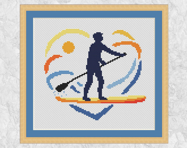 Paddleboarding Heart cross stitch pattern. Silhouette of SUP paddleboarder in sunset and water heart shape. Shown in frame.
