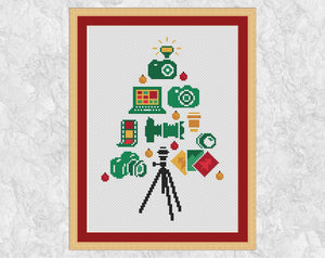 Photographers' Christmas Tree cross stitch pattern: the tree features four cameras, two camera lenses, film negatives, a laptop and photo prints. The flash of one of the cameras forms the Christmas tree star, and a tripod forms the base of the tree. Shown with frame.