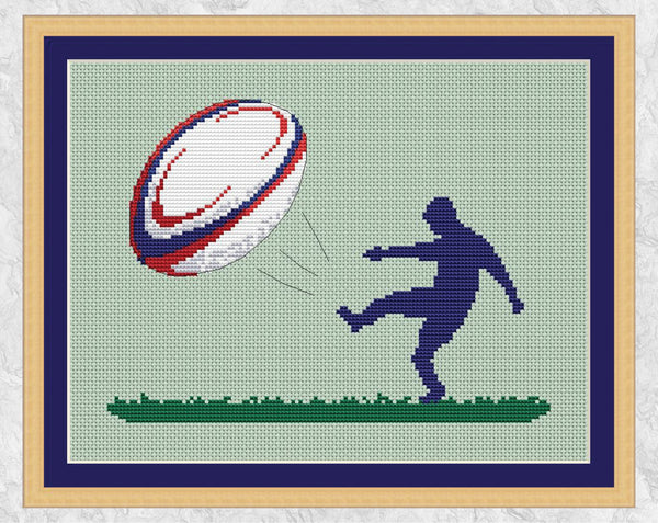 Cross stitch pattern of the silhouette of a rugby player kicking a large colourful rugby ball. Shown with frame.