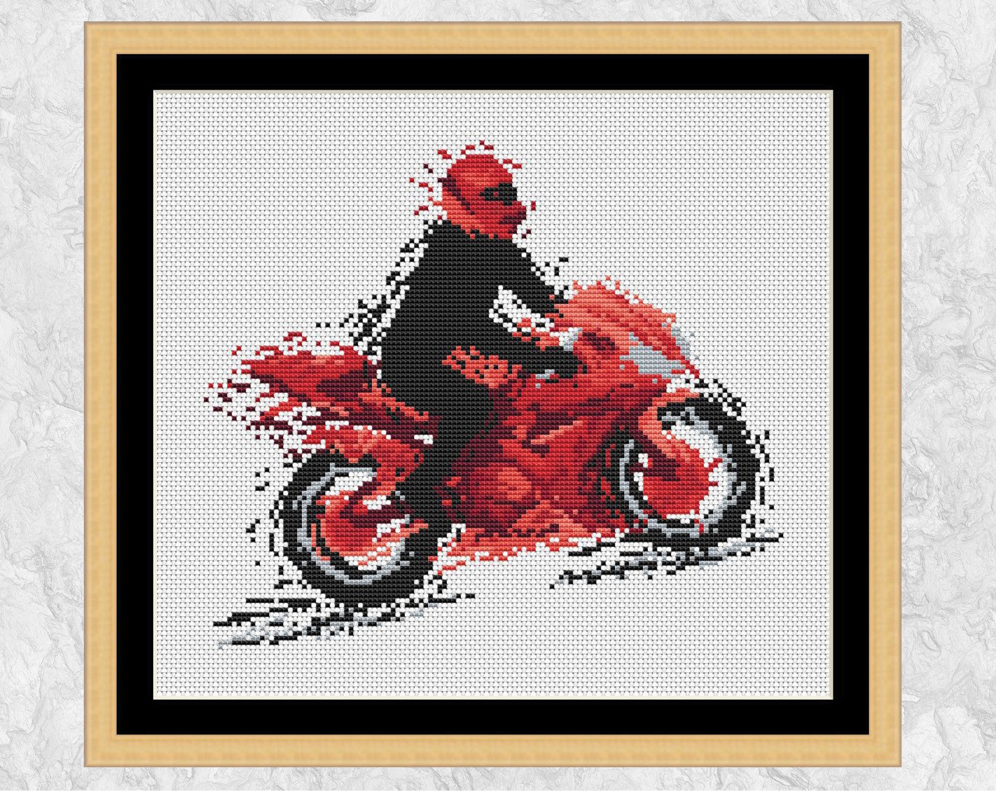 Modern art motorbike cross stitch pattern. The silhouette of a motorcyclist on a red motorbike, all in splattered paint style. Shown in frame with black mount.