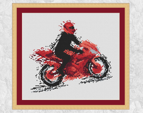 Modern art motorbike cross stitch pattern. The silhouette of a motorcyclist on a red motorbike, all in splattered paint style. Shown in frame with red mount.