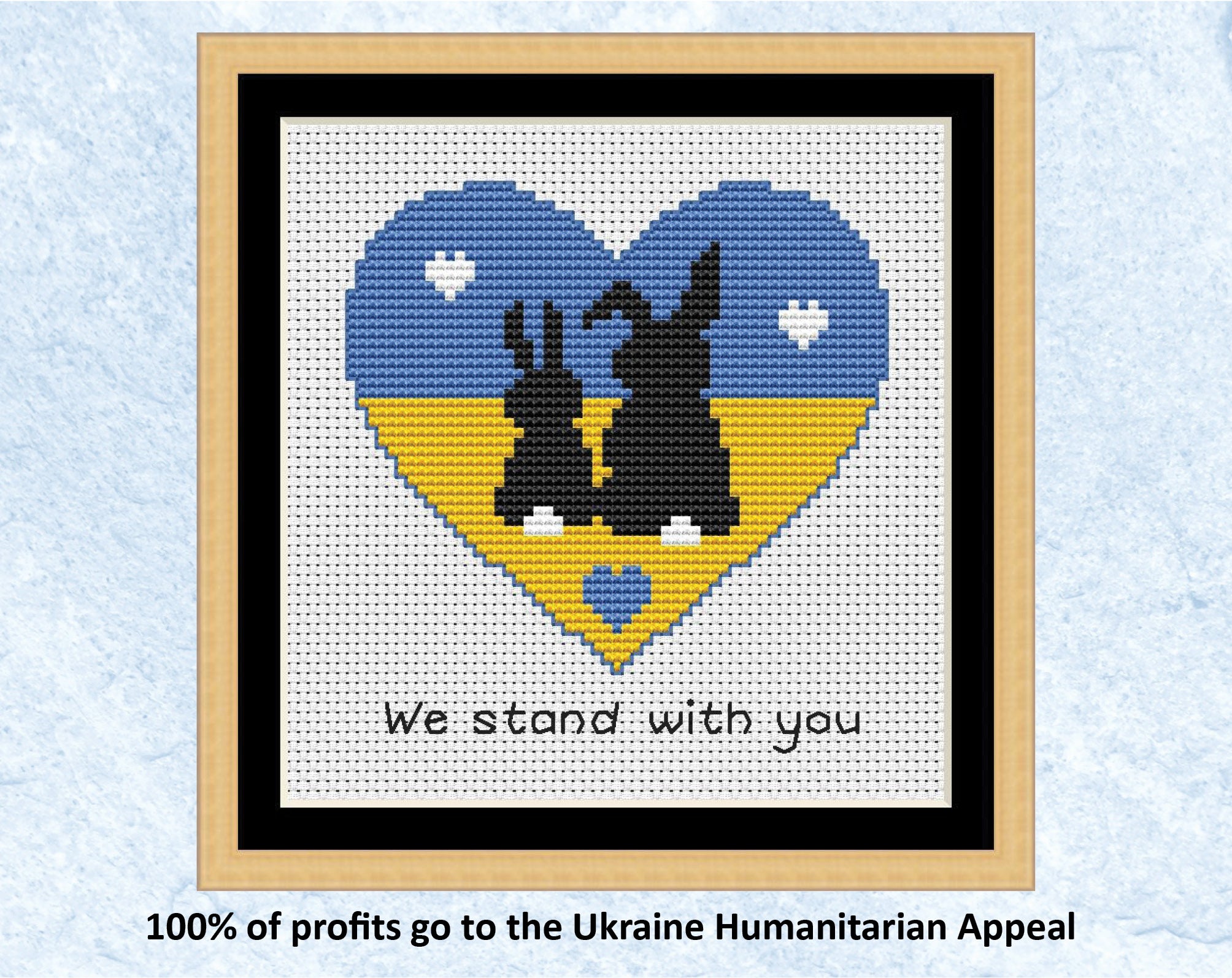 "We Stand With You" cross stitch pattern of two bunnie silhouettes in a heart shape filled with the colours of the Ukrainian flag. 100% of profits go to the Ukraine Humanitarian Appeal. Shown with frame.