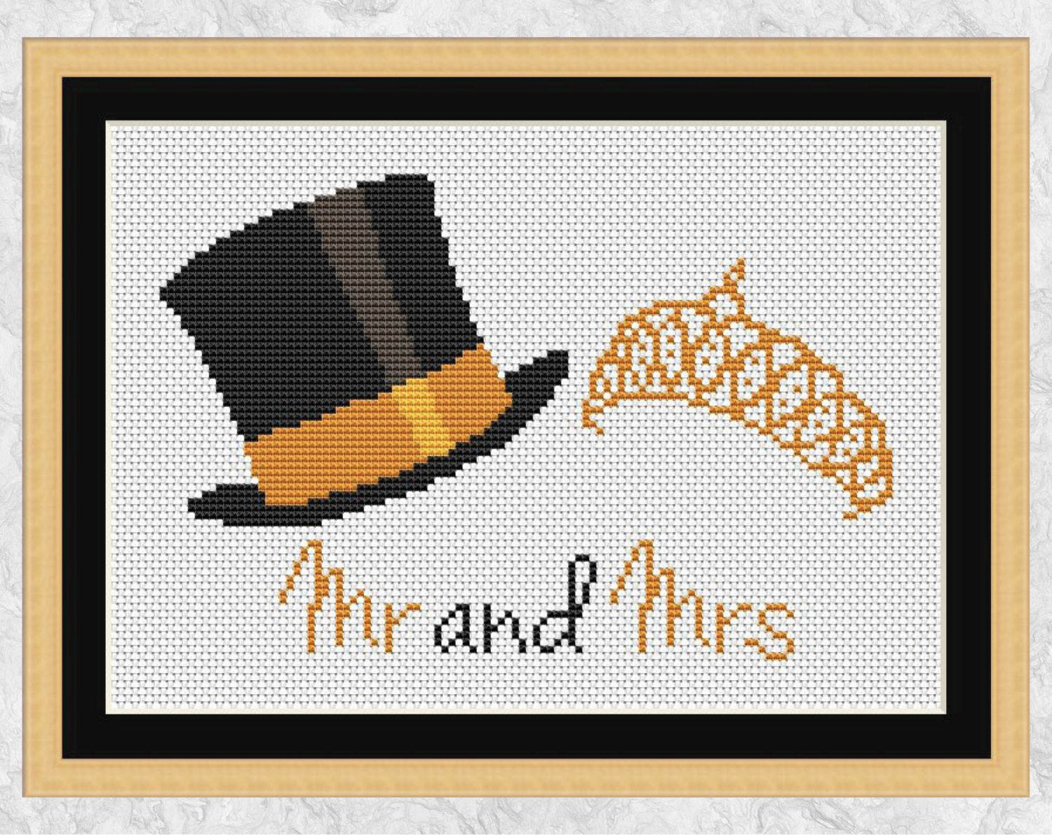 Wedding cross stitch pattern of a top hat and a tiara with "Mr and Mrs" written beneath it. Shown with frame.