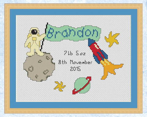 Custom cross stitch pattern of an astronaut holding a flag which will feature a name of your choice. An example name and birth details are shown in the image. Shown with frame.