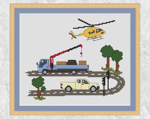 Cross stitch pattern of a road with a truck with a crane, a pickup truck, traffic lights and trees, and a helicopter flying overhead. Shown with frame.