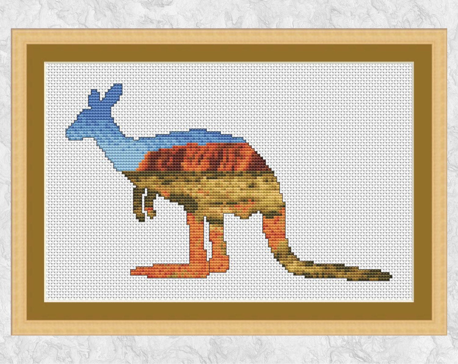 Cross stitch pattern of the silhouette of a Kangaroo filled with a view across the Australian outback to Uluru (Ayers Rock). Shown with frame.