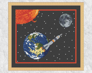 'To the Moon' - Space cross stitch pattern showing rocket, Earth, Sun and Moon. Shown on black fabric with frame.