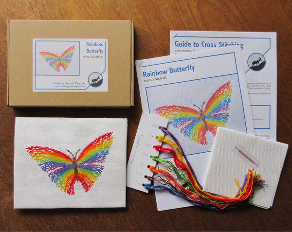 Rainbow Butterfly cross stitch kit - picture of kit contents: labelled box, guide to cross stitching, cross stitch pattern, sorted DMC threads, fabric and needle.