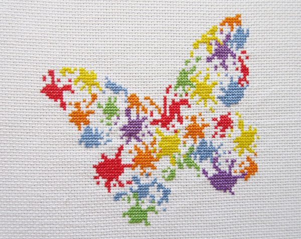 Fun cross stitch pattern of a butterfly made up of splashes of rainbow coloured 'paint'.
