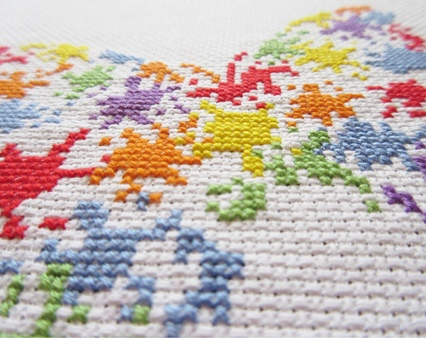 Fun cross stitch pattern of a butterfly made up of splashes of splattered paint - angled view of stitched piece.