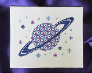 Geometric Saturn - Space cross stitch pattern - stitched and displayed with a purple fabric background