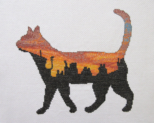 Cross stitch pattern of the silhouette of a cat filled with a scene of a rich and vibrant sunset over city rooftops. Stitched piece.