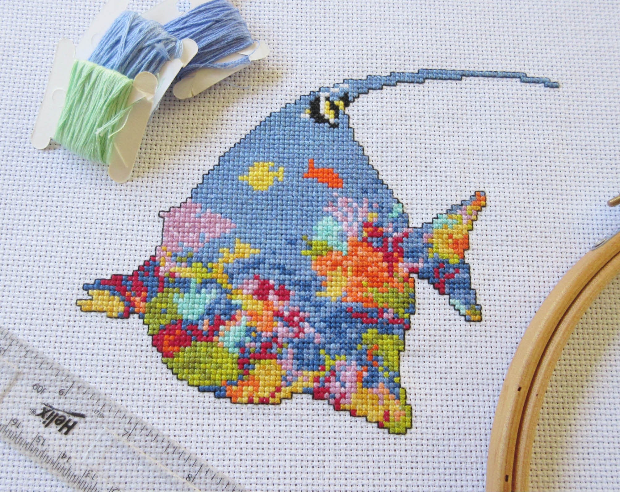 Cross stitch pattern of the silhouette of a tropical fish (a moorish idol fish) filled with a scene of a coral reef. Stitched piece with props.