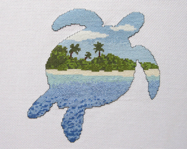 Cross stitch pattern of the silhouette of a turtle filled with a view of a desert island beach, blue sea and sky. Straight view of stitched piece.