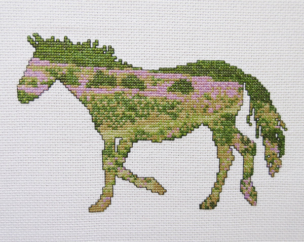 Cross stitch pattern of the silhouette of a pony with a view of the New Forest in southern England inside it. Straight  view of stitched piece.