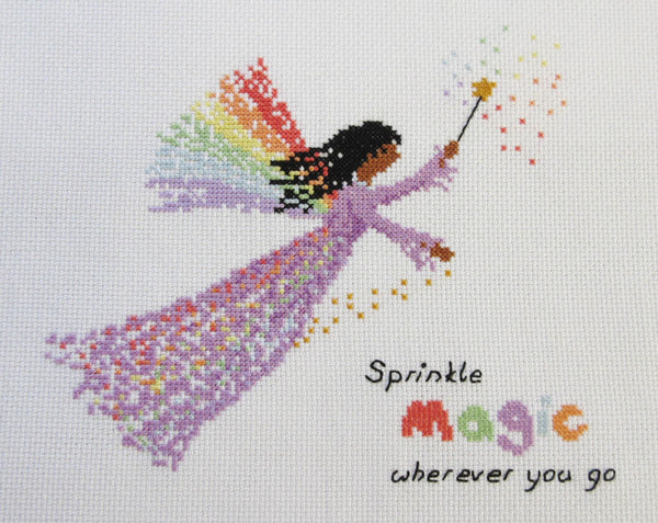 Rainbow Fairy cross stitch pattern - fairy in a purple dress with a wand and wings made of rainbows, and the text 'sprinkle magic wherever you go'. Stitched piece.