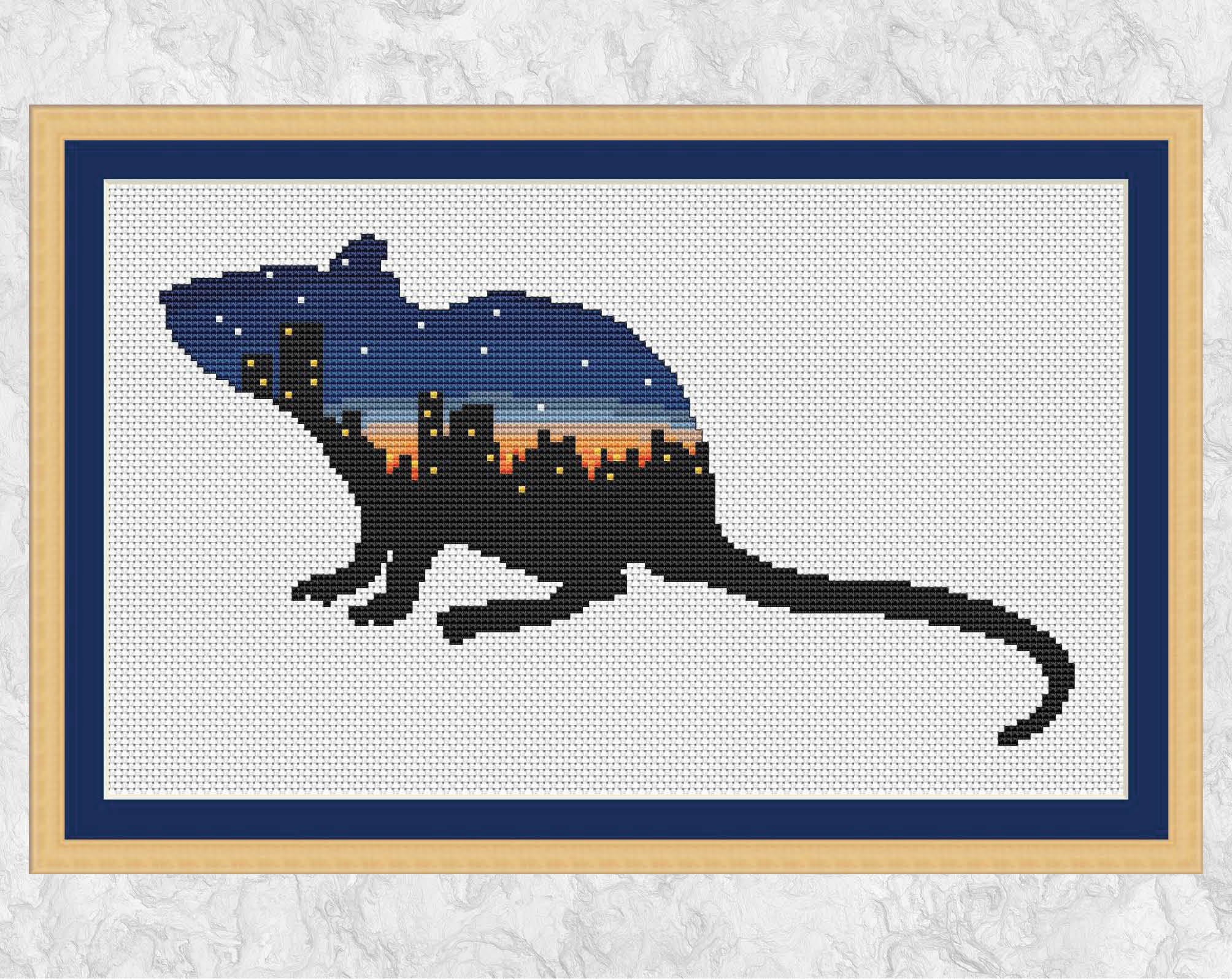 Cross stitch pattern of the silhouette of a rat filled with the scene of a city at twilight. With frame.