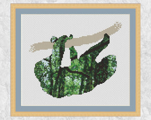 Evocative cross stitch pattern of a sloth filled with a scene of the rainforest, full of trees, leaves and tangled vines. Shown with frame.