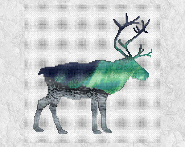 Cross stitch pattern of the silhouette of a reindeer, filled with a scene of the Northern Lights over an Arctic landscape of snow and mountains. Shown without frame.