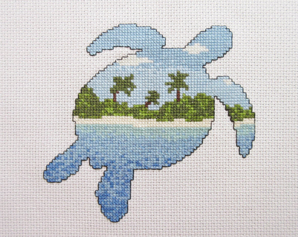 Cross stitch pattern of the silhouette of a turtle filled with a view of a desert island beach, blue sea and sky. Straight view of stitched piece.