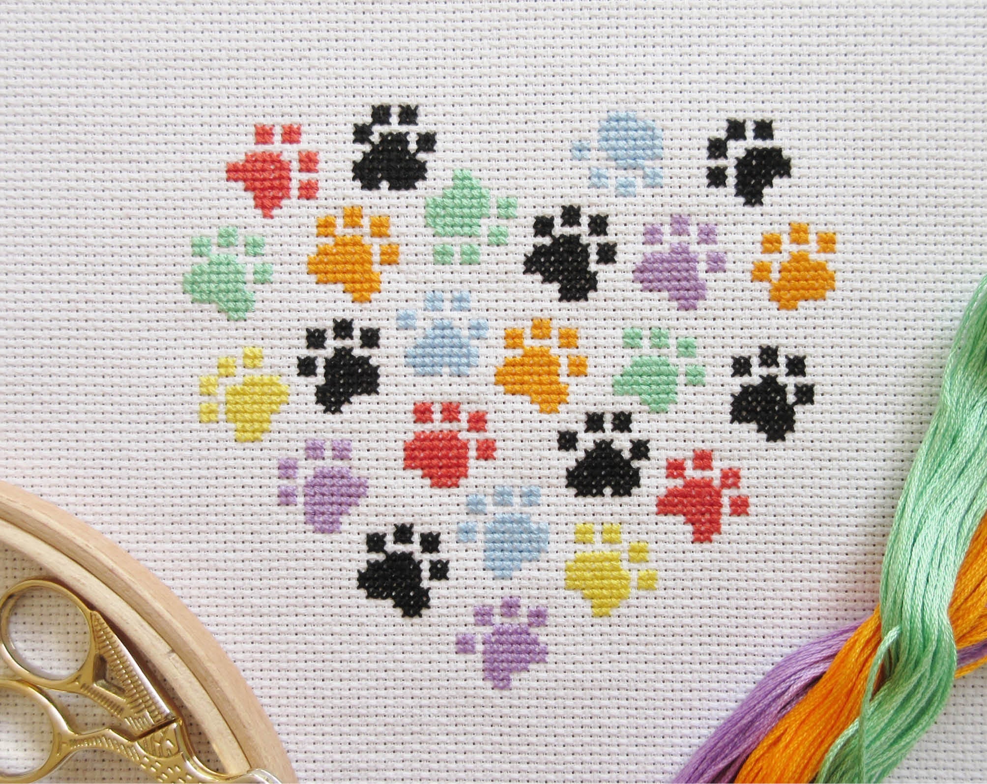Stitched image of smaller paw print heart cross stitch pattern, with stitching materials