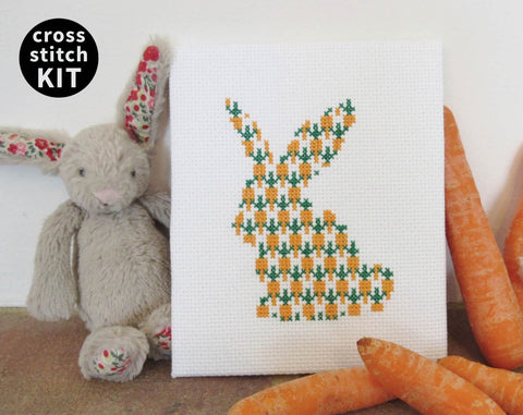 Carrot Bunny cross stitch kit - silhouette of a rabbit filled with carrots. Image shows stitched piece with toy rabbit and real carrots.