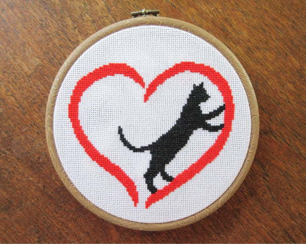 Cross stitch pattern PDF of a cat climbing inside a heart - stitched piece in hoop on wooden background