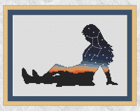 Cross stitch pattern of the silhouette of a woman, filled with the zodiac constellation of Virgo above a sunset. Shown with frame.